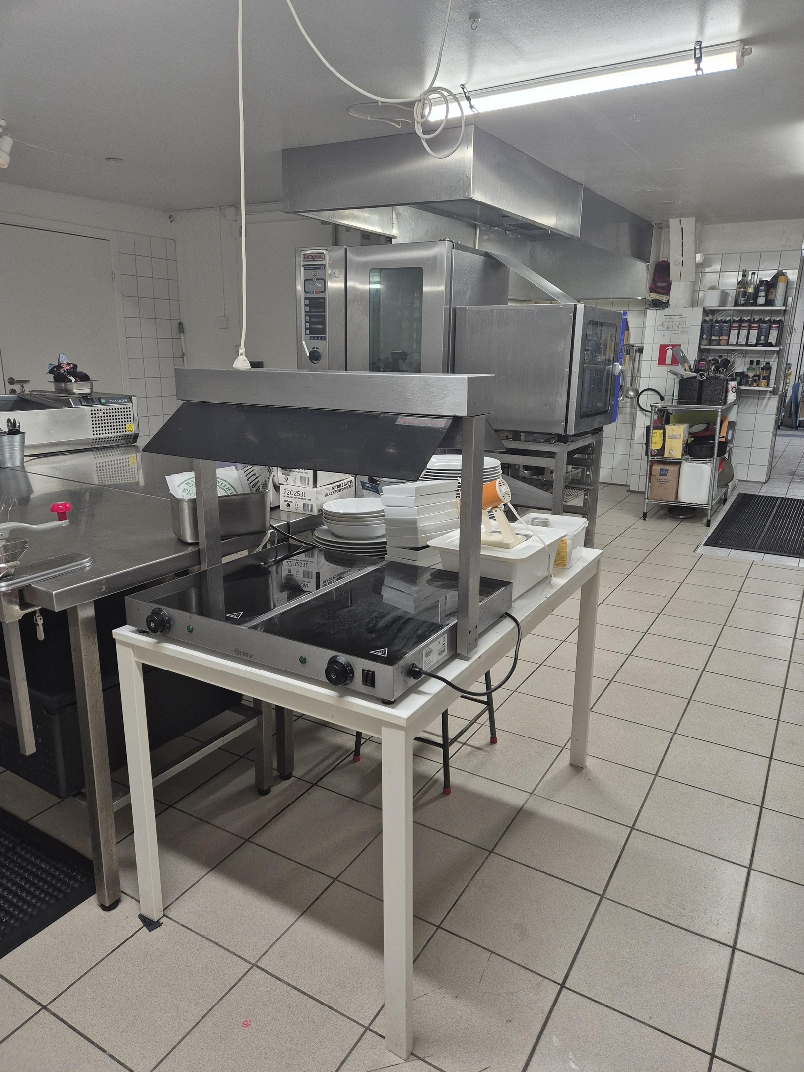 A chef wearing gloves works with cooking equipment in a busy restaurant kitchen preparing meals for customers during dinner service.